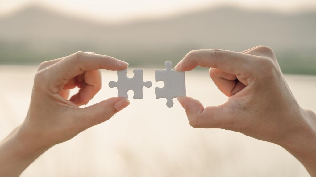 woman and man hand connecting a piece of jigsaw puzzle on mountain and lake background. symbol of association and connection concept. business strategy.
